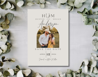 Puede incluir: Una tarjeta de guardar la fecha con un tema rústico. La tarjeta presenta una foto de una pareja frente a un campo, con un diseño de herradura y el texto "HUM HUNTER AND MEGAN Anderson SAVE THE DATE APRIL 12 2024 Formal invitation to follow."