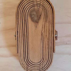 May include: A wooden nesting bowl set with a natural wood finish. The bowl is made of multiple layers of wood that are stacked on top of each other. The bowl is oval shaped and has a smooth surface.
