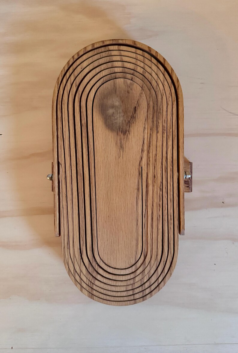 May include: A wooden nesting bowl set with a natural wood finish. The bowl is made of multiple layers of wood that are stacked on top of each other. The bowl is oval shaped and has a smooth surface.