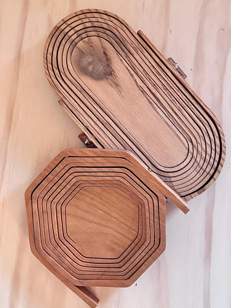 May include: Two wooden serving trays, one oval and one octagonal, are stacked on a wooden surface. Both trays are made of multiple layers of wood, creating a unique and rustic look.