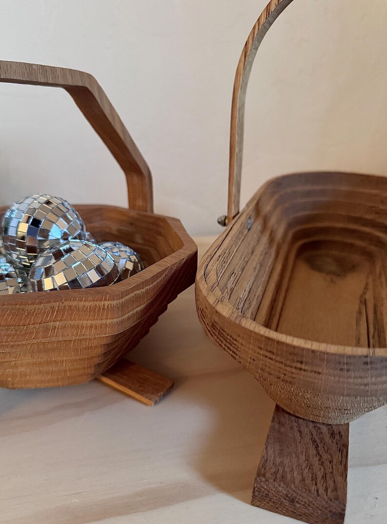 May include: Two wooden baskets with handles. One basket is filled with silver disco balls. Both baskets have a natural wood finish and stand on small wooden feet.