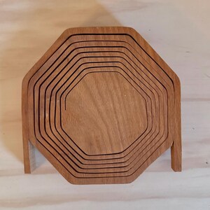 May include: A set of eight wooden octagonal nesting trays. The trays are made of light brown wood and are stacked on top of each other.