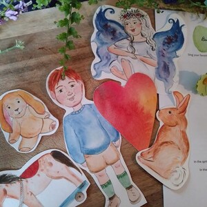 Może przedstawiać: Zestaw kolorowych wycinanek z papieru do zabawy dla dzieci. Zestaw zawiera chłopca, dziewczynkę z skrzydłami, kr&oacute;lika, psa, konika na biegunach, serce i kartkę papieru z instrukcjami do gry o tematyce kr&oacute;liczej.
