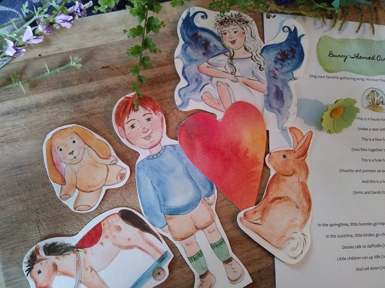 Może przedstawiać: Zestaw kolorowych wycinanek z papieru do zabawy dla dzieci. Zestaw zawiera chłopca, dziewczynkę z skrzydłami, kr&oacute;lika, psa, konika na biegunach, serce i kartkę papieru z instrukcjami do gry o tematyce kr&oacute;liczej.