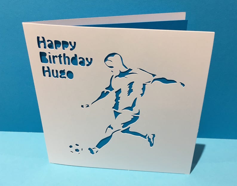 May include: White card with a silhouette of a soccer player kicking a ball. The card says "Happy Birthday Hugo" in a decorative font.