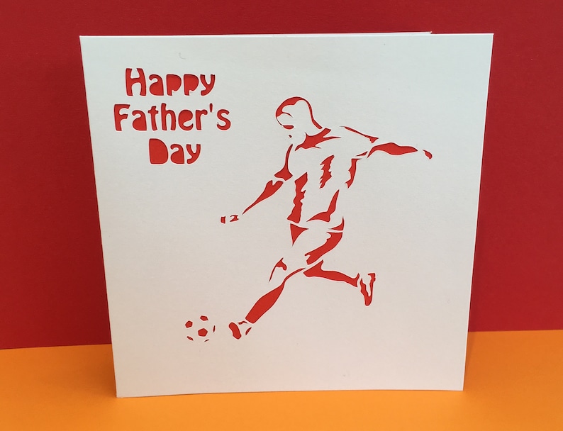 May include: A white card with red text that says "Happy Father's Day". A red silhouette of a soccer player kicking a ball is on the card.