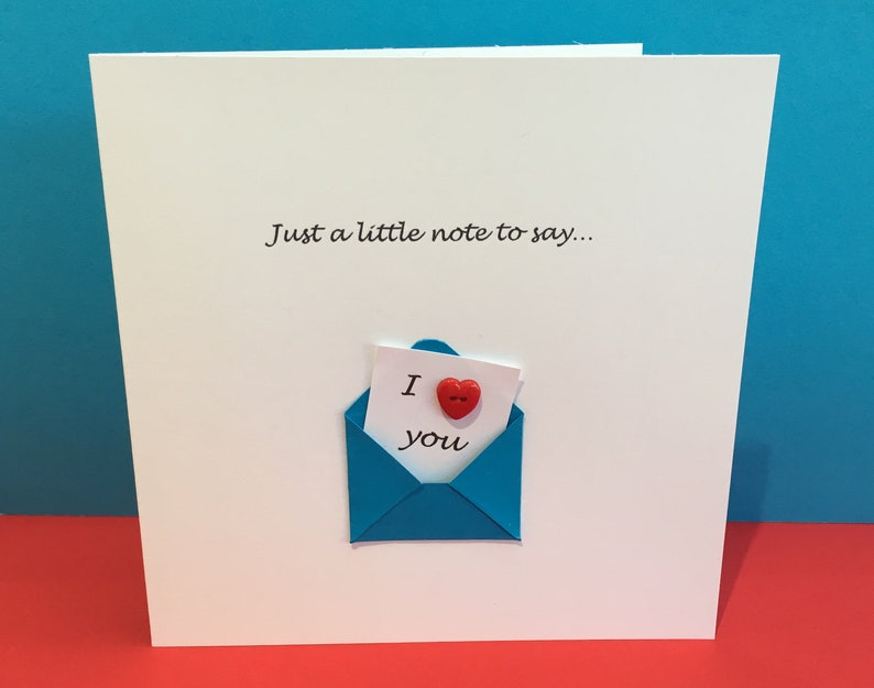 May include: A white card with the text "Just a little note to say..." and a blue envelope with a red heart button and the text "I love you" inside.