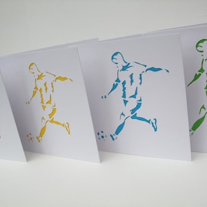 May include: Four white cards with a silhouette of a soccer player kicking a ball. The players are cut out and colored in red, yellow, blue, and green.