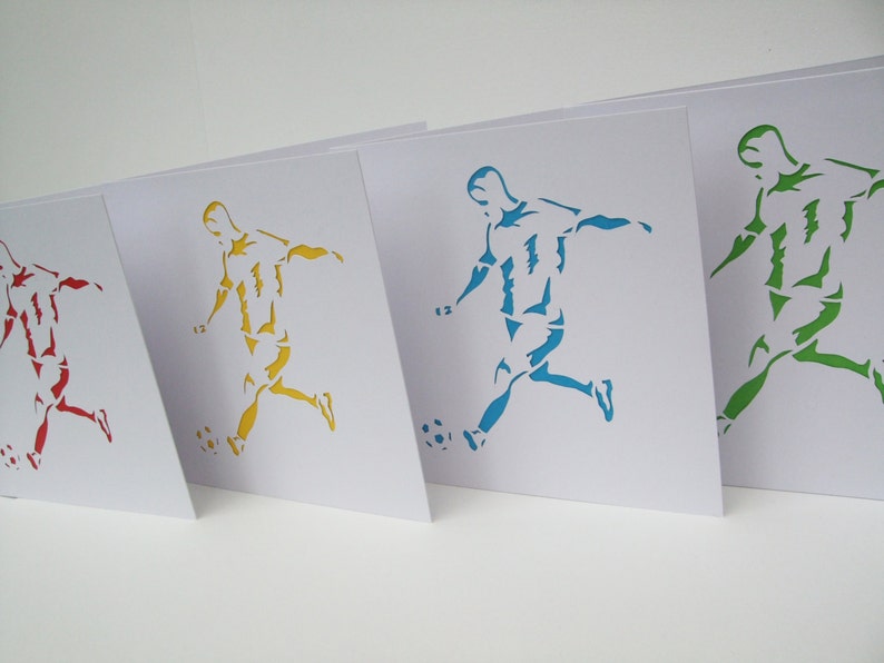 May include: Four white cards with a silhouette of a soccer player kicking a ball. The players are cut out and colored in red, yellow, blue, and green.