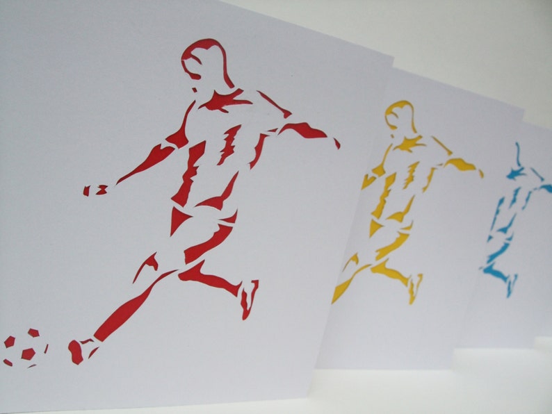 May include: Three paper cutouts of a soccer player kicking a ball. The player on the left is red, the middle player is yellow, and the player on the right is blue.