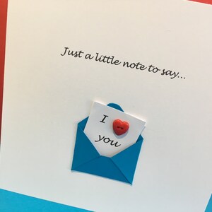 May include: A white card with the text "Just a little note to say..." and a blue envelope with a white note inside that says "I love you" with a red heart button.