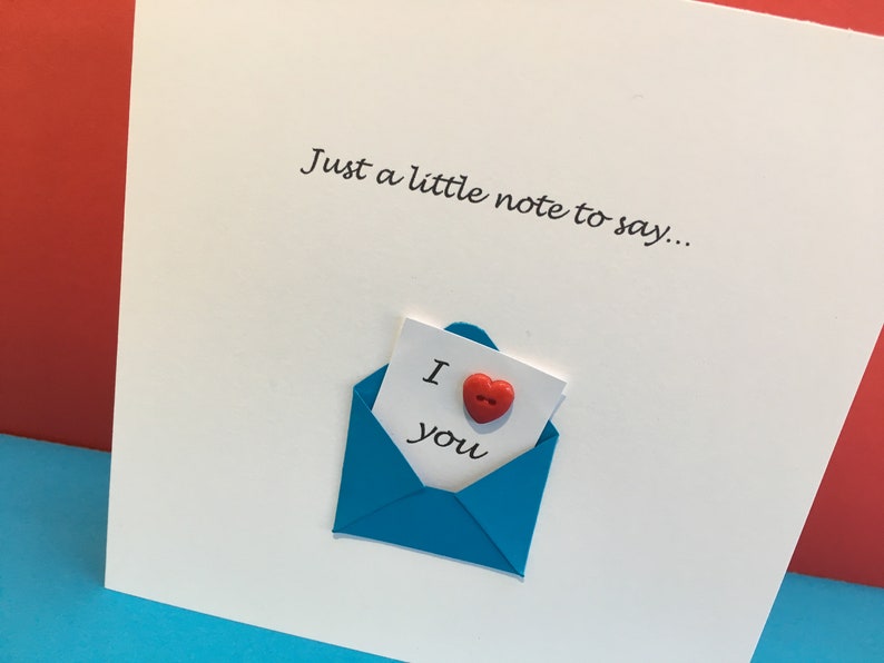 May include: A white card with the text "Just a little note to say..." and a blue envelope with a white note inside that says "I love you" with a red heart button.