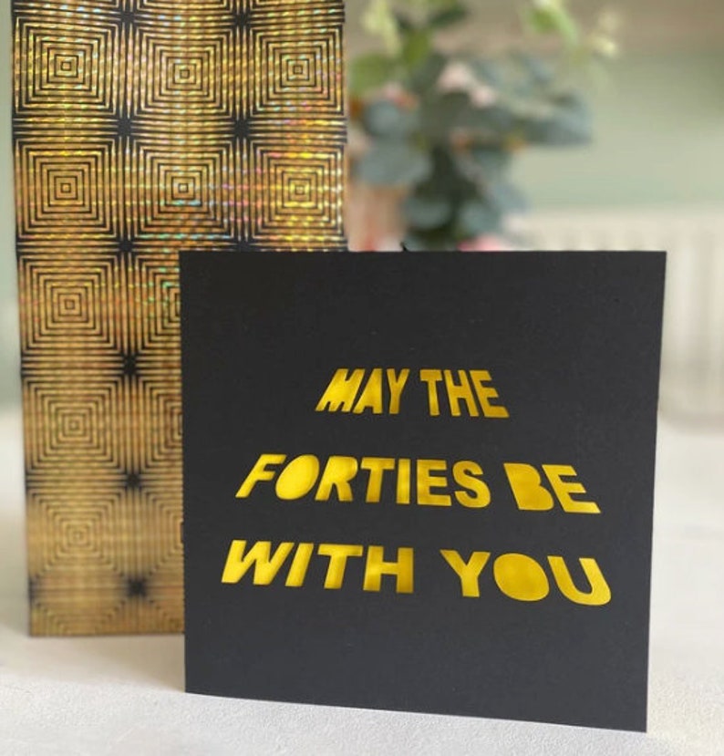 May include: A black card with gold lettering that reads "May the Forties Be With You".