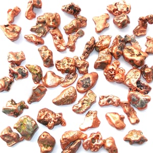 May include: A collection of copper nuggets, some with a greenish patina, on a white background. The nuggets are various shapes and sizes, with some being more rounded and others more irregular.