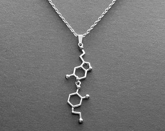 Könnte beinhalten: Eine silberne Halskette mit einem Anhänger in Form einer chemischen Struktur. Der Anhänger ist eine 3D-Darstellung eines Moleküls.