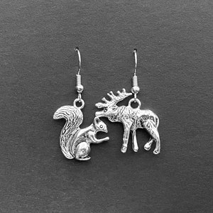 May include: Silver earrings featuring a moose and squirrel design. The moose is standing on all fours and the squirrel is sitting upright.