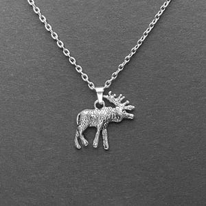 Peut inclure: Un collier en chaîne argent avec un pendentif en forme d'élan en argent. L'élan est debout, la tête tournée sur le côté et les bois levés.