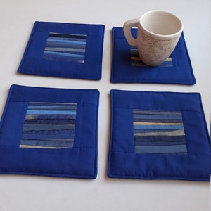 Peut inclure: Ensemble de quatre dessous-de-verre en tissu bleu avec un motif rayé dans des tons de bleu et de beige. Les dessous-de-verre sont carrés et ont une bordure cousue.