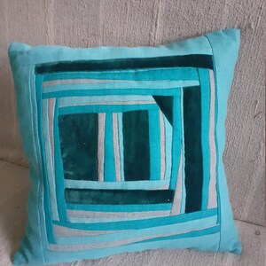 Op de afbeelding: Een turquoise blauw kussen met een geometrisch patroon van strepen en vierkanten in tinten turquoise, groen en grijs.