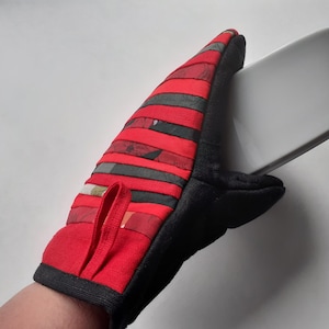 May include: Red and black oven mitt with a striped pattern. The mitt is made of fabric and has a loop for hanging.