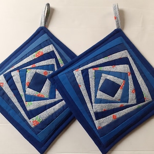 Peut inclure: Deux maniques de cuisine matelassées bleu et blanc avec un motif en spirale et des accents floraux rouges. Les maniques ont une boucle pour accrocher.