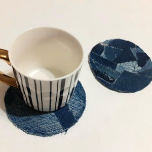 Könnte beinhalten: Zwei Untersetzer aus blauem Jeansstoff mit einer weiß-schwarz gestreiften Tasse auf einem der Untersetzer.