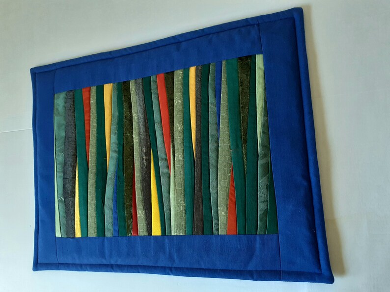 May include: A blue fabric wall hanging with a colorful striped design. The stripes are made of different fabrics and colors, including green, yellow, red, and brown.