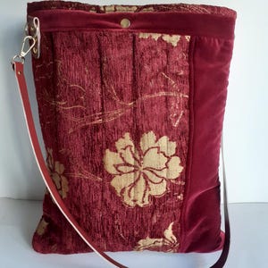 Może przedstawiać: Bordowa torba typu tote ze złotym kwiatowym wzorem. Torba ma aksamitne wykończenie i skórzany pasek. Torba ma około 35 cm wysokości i 30 cm szerokości.