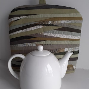 Pode incluir: Um conjunto de três canecas de cerâmica com acabamento fosco e salpicado. As canecas são em tons de creme, cinza claro e cinza escuro. Cada caneca tem um design simples e minimalista.