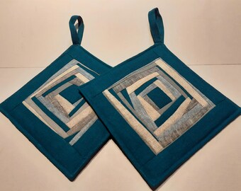 May include: Two teal square pot holders with a geometric design. The center features a square pattern of gray, light gray, and beige fabric strips. Each pot holder has a teal loop for hanging.