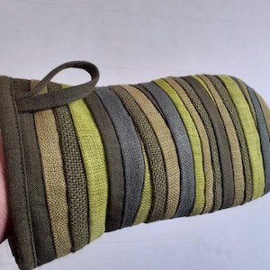 May include: An oven mitt with a loop for hanging. The mitt features vertical stripes in shades of green, gray, and brown. The stripes are sewn together, creating a textured surface. The cuff and loop are a solid dark green.