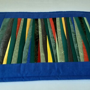 May include: A blue quilted placemat with a colorful striped design in shades of green, yellow, red, and black.