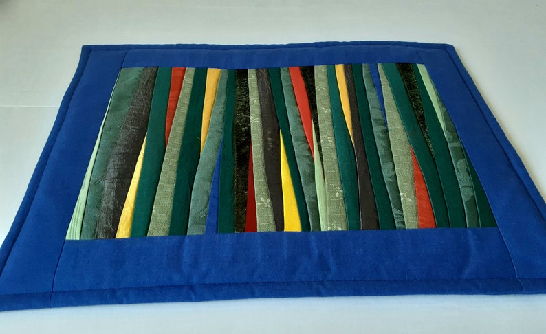 May include: A blue quilted placemat with a colorful striped design in shades of green, yellow, red, and black.