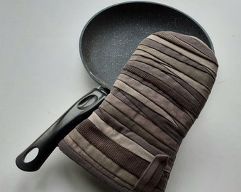 Könnte beinhalten: Eine schwarze Antihaft-Bratpfanne mit langem Griff und einem braunen gestreiften Ofenhandschuh.