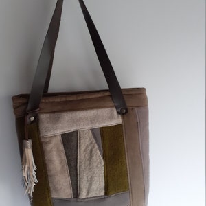 Może przedstawiać: Brązowa torba typu tote z patchworku ze skórzanymi uchwytami i frędzlami. Torba jest wykonana z różnych odcieni brązowego i zielonego materiału.