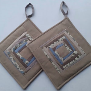 Può includere: Due presine da forno imbottite di colore marrone con un motivo geometrico in tessuto beige, marrone, blu e bianco. Le presine hanno un'ansa a forma di anello.