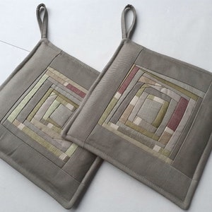 Op de afbeelding: Twee grijze, gestikte ovenwanten met een vierkant ontwerp in tinten groen, beige en roze.