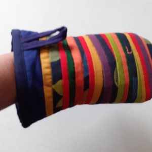 May include: A colourful oven mitt with vertical stripes in various colours, including red, orange, yellow, green, and purple. The cuff is navy blue with a loop for hanging. The mitt is designed for kitchen use.