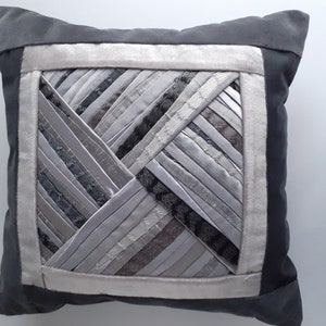 May include: A gray throw pillow with a white border and a geometric pattern of silver and gray fabric strips.