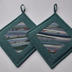 Może przedstawiać: Dwa tealowe, pikowane uchwyty do garnków z paskowanym środkiem z tkaniny. Tkanina jest połączeniem niebieskiego, zielonego i białego.