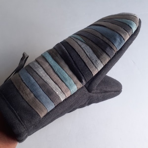 Könnte beinhalten: Ein schwarzer Ofenhandschuh mit einem gestreiften Design in Blautönen, Grau und Braun. Der Handschuh hat eine Schlaufe zum Aufhängen.