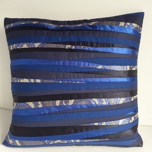 Op de afbeelding: Blauw en zwart gestreept kussen met een golvend ontwerp. Het kussen is gemaakt van stof met een satijnachtige afwerking.