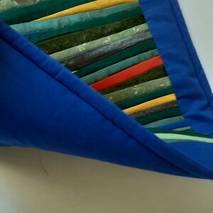 May include: A blue fabric bag with a colorful striped fabric lining. The lining is made of various shades of green, yellow, and red.