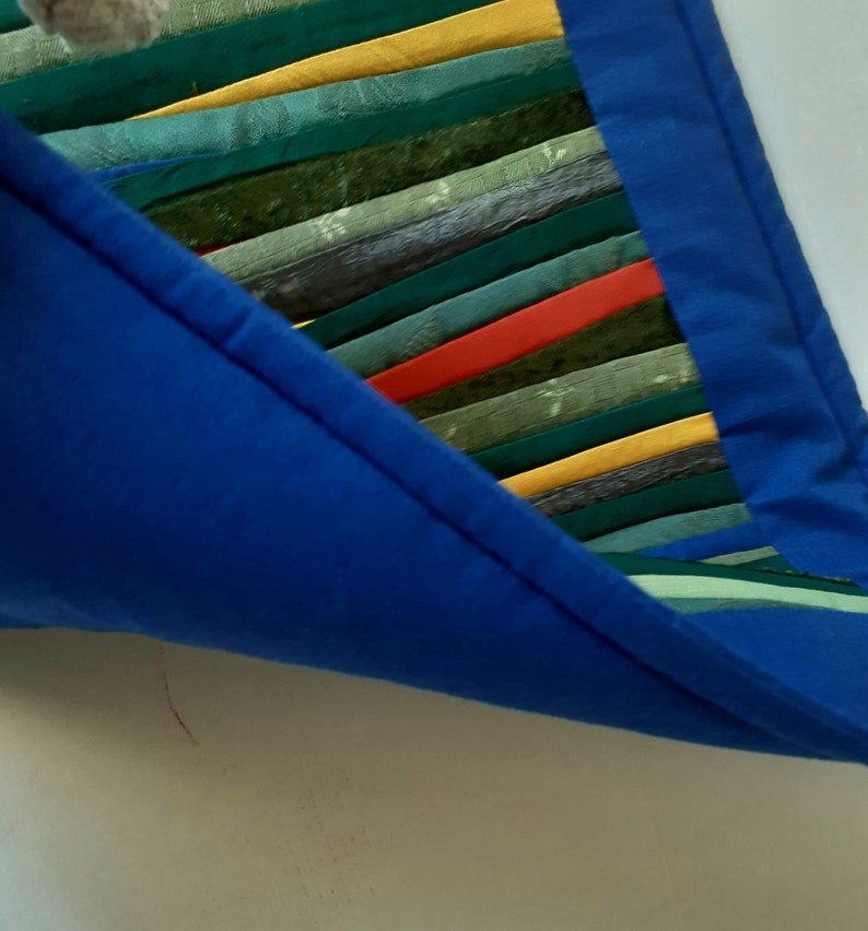 May include: A blue fabric bag with a colorful striped fabric lining. The lining is made of various shades of green, yellow, and red.