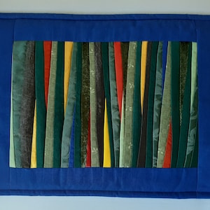 May include: A blue fabric placemat with a border and a center panel made of colorful fabric strips. The strips are arranged vertically and are in shades of green, yellow, red, and black.