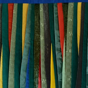 May include: A close-up of a fabric wall hanging made of strips of fabric in various shades of green, blue, yellow, and red. The fabric strips are sewn together to create a vertical pattern.