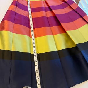 May include: A pleated skirt with horizontal stripes in vibrant colors: purple, orange, yellow, and navy blue. The skirt measures approximately 28 inches in length. The skirt has a navy blue waistband.