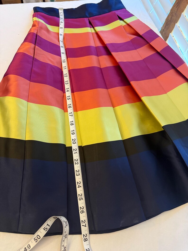 May include: A pleated skirt with horizontal stripes in vibrant colors: purple, orange, yellow, and navy blue. The skirt measures approximately 28 inches in length. The skirt has a navy blue waistband.