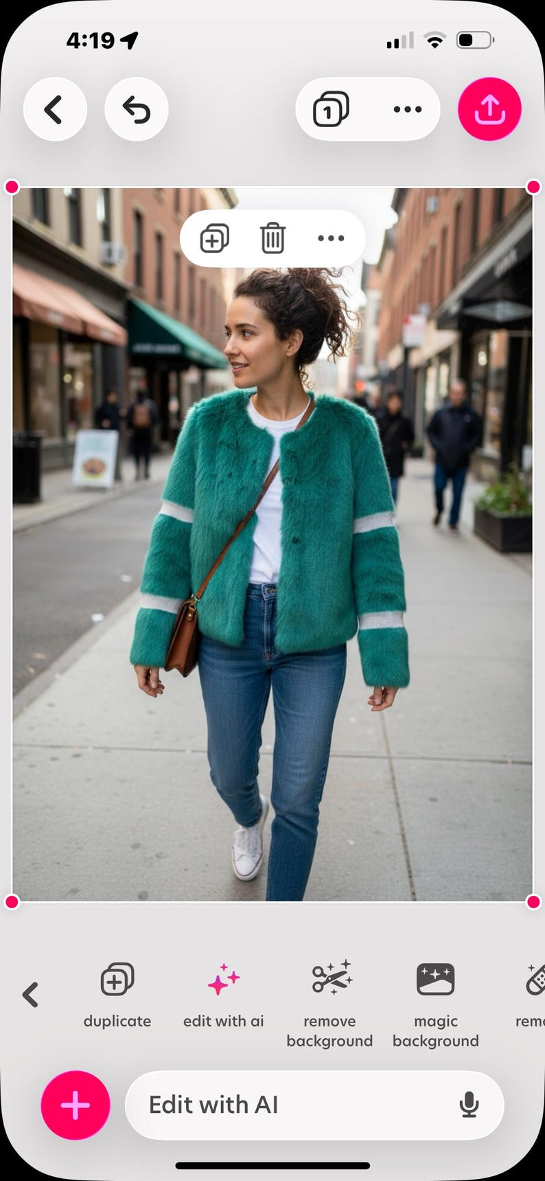 Op de afbeelding: Een vrouw draagt een teal imitatiebontjas met witte strepen op de mouwen en zoom, gecombineerd met een blauwe jeans en witte sneakers. Ze draagt een bruine tas en loopt op een stoep.