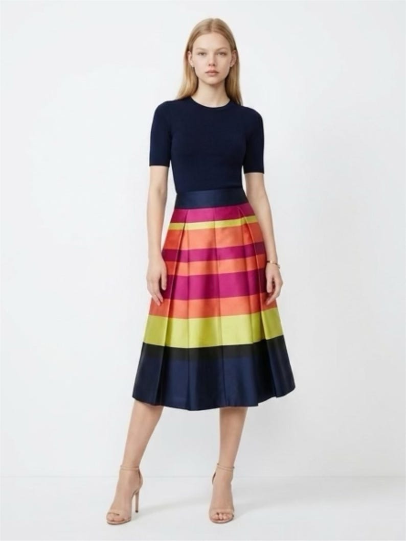 May include: A navy blue short-sleeve top paired with a vibrant, pleated midi skirt. The skirt features horizontal stripes in shades of pink, orange, yellow, and navy blue. The model is wearing nude-colored heels.